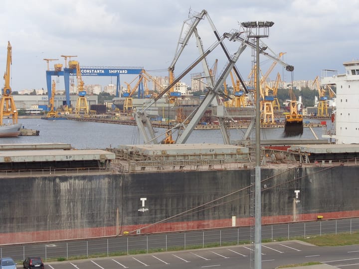 Navă de mărfuri încărcată cu cărbune în Portul Constanța, cu macarale și șantierul naval în fundal